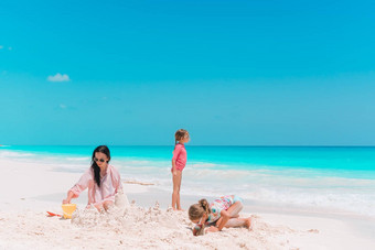 家庭使沙子城堡热带白色海滩妈妈。女孩玩沙子热带海滩