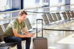 乘客机场休息室等待飞行飞机年轻的男人。手机机场等待着陆
