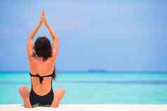 健康的年轻的女人坐着瑜伽位置冥想海滩