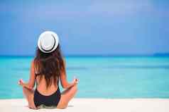 健康的年轻的女人坐着瑜伽位置冥想海滩