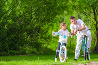 年轻的父亲女孩骑自行车夏天温暖的一天年轻的活跃的家庭骑自行车