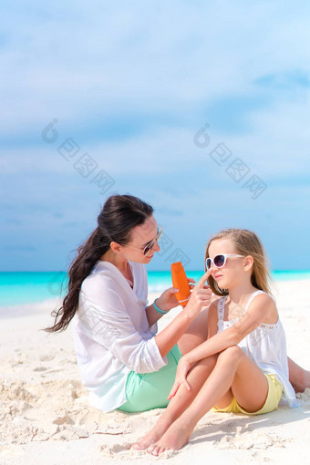 年轻的妈妈。应用太阳奶油女儿鼻子海滩概念保护紫外线辐射