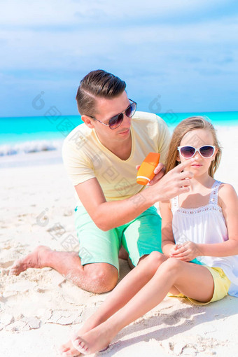 有爱心的父亲应用太阳奶油女儿鼻子海滩概念保护紫外线辐射