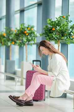年轻的女人国际机场行李智能手机等待飞行