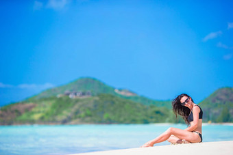 女人坐着海滩笑享受夏天假期相机美丽的模型比基尼坐着
