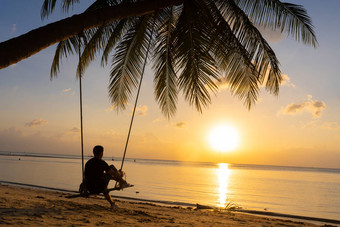 的家伙享受日落骑摇摆不定的热带海滩轮廓的家伙摇摆不定的挂棕榈树看日落水
