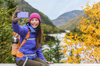 快乐亚洲徒步旅行者女人采取智能手机自拍风景优美的的观点自然秋天山景观在户外女孩徒步旅行秋天森林公园旅行生活方式女孩持有电话