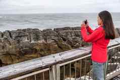 新西兰旅行旅游女孩采取智能手机图片电话应用程序红色分配煎饼岩石女人paparoa国家公园西海岸南岛新西兰