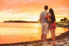 夫妇放松夏天假期旅行站海滩看日落热带目的地轮廓黄昏
