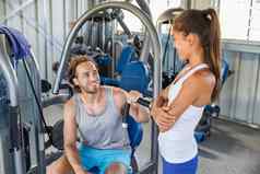 健身健身房教练会说话的男人。培训锻炼设备机在室内夫妇快乐工作