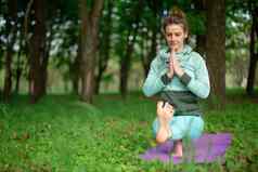 年轻的体育女孩实践瑜伽辞职绿色夏天森林