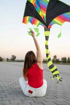 年轻的女人飞行风筝公共公园日落