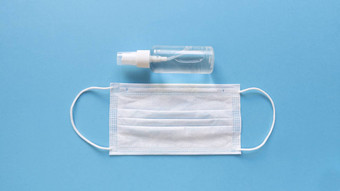 白色医疗面具手洗手液透明的瓶喷雾帽中间蓝色的背景简单的平躺柔和的纸纹理医疗概念股票照片