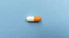 橙色白色单药丸胶囊蓝色的背景简单的平躺柔和的纹理医疗概念股票照片