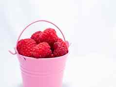 红色的成熟的树莓下降粉红色的桶白色背景