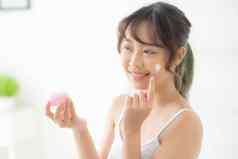 美丽的年轻的亚洲女人快乐应用奶油乳液