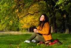 漂亮的女孩享受秋天美自然坐着绿色草坪上公园秋天情绪