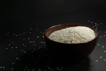 白色未煮过的大米碗分散谷物附近的黑色的背景