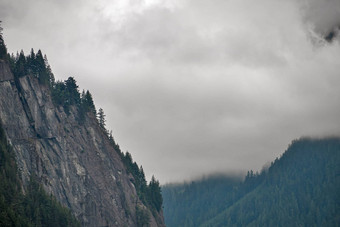 陡峭的岩石山悬崖包围树阴天空背景