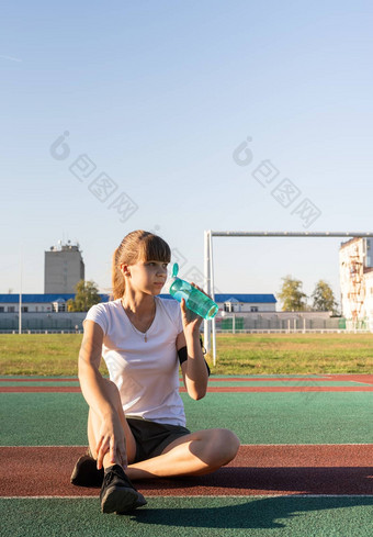 年轻的十几岁的女人坐着体育场喝水工作