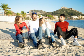 年轻的夫妻海日落海边度假胜地冬天有趣的会说话的笑集团朋友坐着海滩冬天海假期白色红色的服装