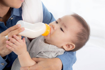 年轻的亚洲妈妈。拥抱喂养婴儿女孩瓶牛奶首页新生儿是清白的喝妈妈满意的关系成键妈妈孩子家庭概念