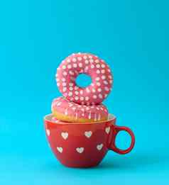 堆栈粉红色的甜甜圈糖衣红色的陶瓷杯蓝色的背景