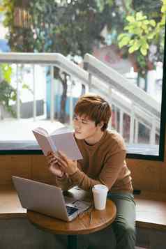 沉思的年轻的亚洲商人阅读书桌面移动PC咖啡杯咖啡商店知识概念