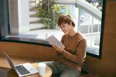 沉思的年轻的亚洲商人阅读书桌面移动PC咖啡杯咖啡商店知识概念