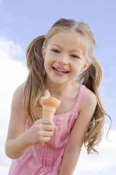 年轻的女孩在户外吃冰奶油锥微笑