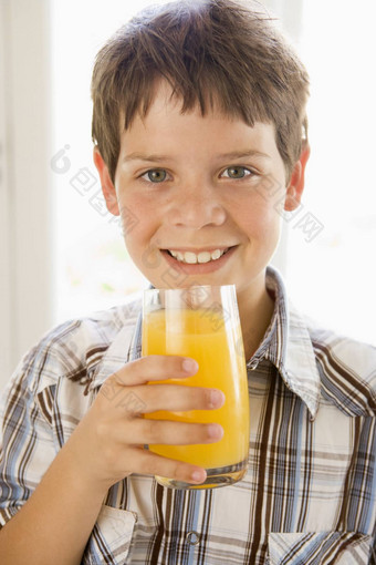 年轻的男孩在室内喝橙色<strong>汁</strong>微笑