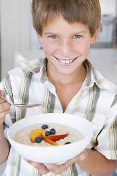 年轻的男孩厨房吃燕麦片水果微笑