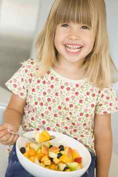 年轻的女孩厨房吃碗水果微笑
