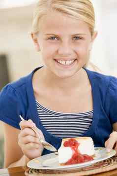 年轻的女孩在室内吃芝士蛋糕微笑