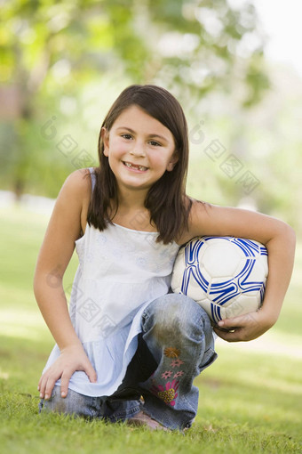 年轻的女孩在户外公园持有球微笑