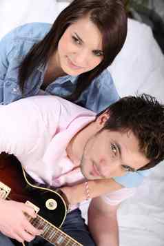 年轻的夫妇床上男人。玩吉他