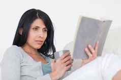 女人持有灰色杯子阅读书
