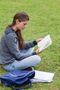 年轻的女孩阅读书坐着盘腿