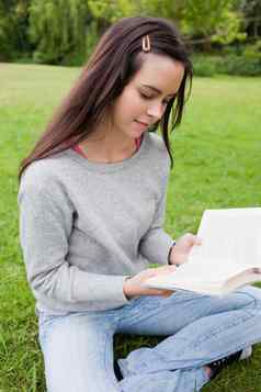 年轻的平静女孩阅读书坐着草