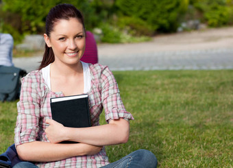 积极的女学生持有书坐着草