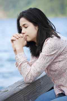 年轻的青少年女孩坐着安静地湖码头祈祷