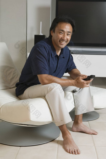 肖像快乐亚洲男人。坐着现代生活房间远程控制前面大屏幕首页