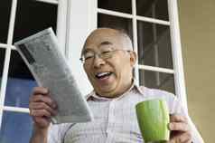 快乐的高级男人。咖啡杯阅读报纸前面房子