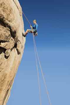 低角视图年轻的女人用绳索下降悬崖清晰的蓝色的天空