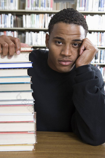 肖像无聊非洲美国大学学生坐着堆栈书图书馆