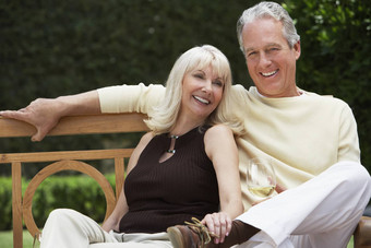 快乐中间岁的夫妇坐着板凳上酒玻璃花园