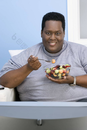 非洲美国肥胖男人。看电视吃<strong>水果首页</strong>