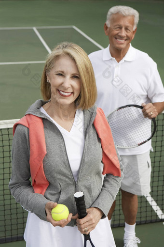微笑夫妇站网球法院持有球拍球