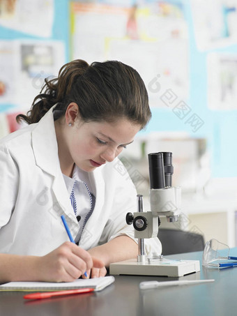 十几岁的女孩显微镜采取笔记实验室
