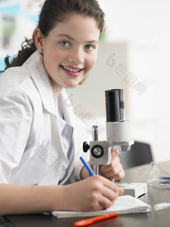 肖像快乐十几岁的女孩显微镜采取笔记实验室